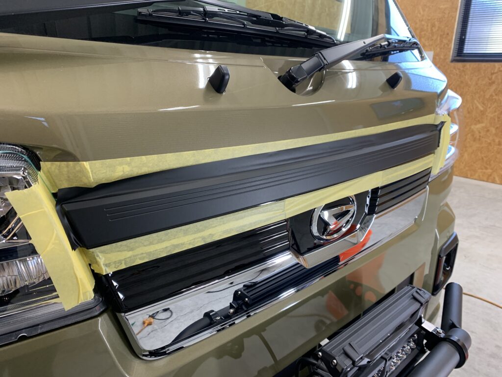 フロントグリルのカーラッピング施工中。塗装保護のためマスキングを施し、ブラックアウトラッピング行っている作業風景。