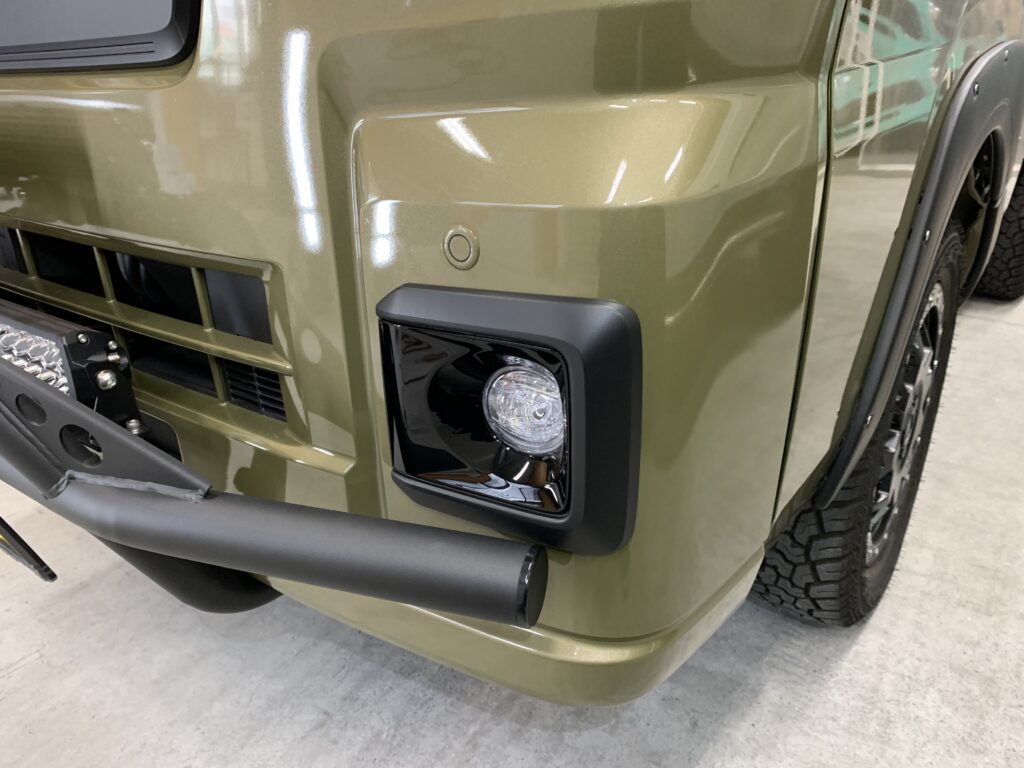 カーラッピング施工後のフロントバンパー。オリーブグリーンのボディにフォグランプ周りをブラックアウトラッピングで仕上げ、力強い印象を強調したカスタム事例。