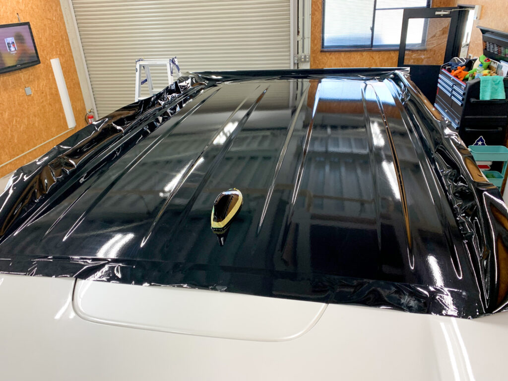 ランドクルーザー300のルーフラッピング施工中の様子。ブラックフィルムをルーフへ貼り込みしている作業風景。