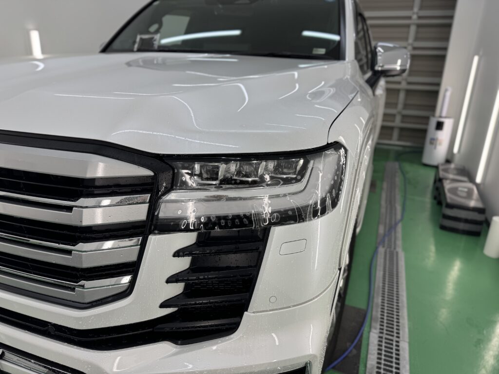 ランドクルーザー300のヘッドライトへプロテクションフィルム施工中の様子。施工液が残った状態で、フィルムを丁寧に貼り込んでいる工程写真。