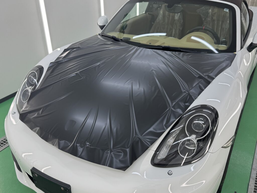 ポルシェ981型ボクスターのボンネットへ3Mサテンブラックを施工している様子