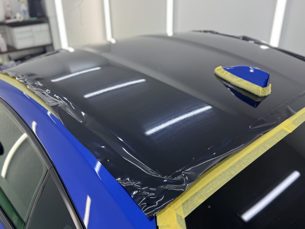 SUBARU BRZのルーフへブラック系ラッピングフィルムを施工している途中の写真。ルーフアンテナ周辺まで丁寧にフィルムを貼り込んでいる様子