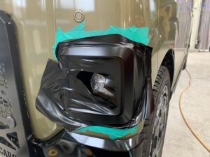 カーキメタリックのスバル ディアスのフォグランプベゼル部分にブラックラッピングを施工中の様子。立体形状に合わせてフィルムを丁寧に貼り込んでいる。