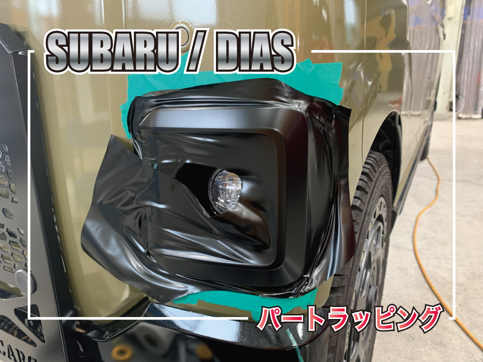 カーキメタリックのスバル ディアスのフォグランプ周辺にブラックラッピングフィルムを施工している様子。ボディカラーとのコントラストでフロントフェイスを引き締めるパートラッピング施工。