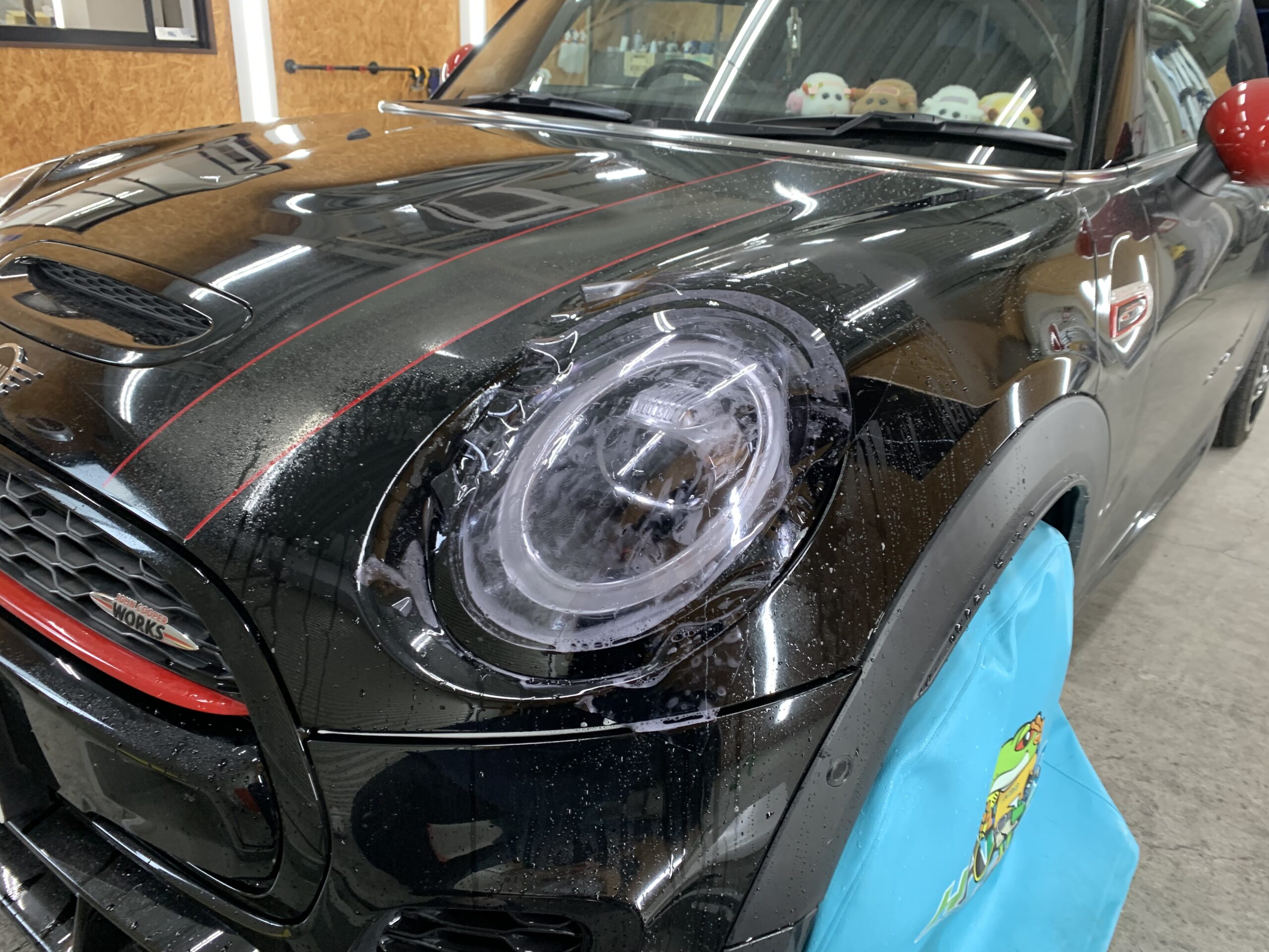 MINI JCWのヘッドライトにプロテクションフィルムを施工している様子。施工液を使用しながら貼り込みを行う工程