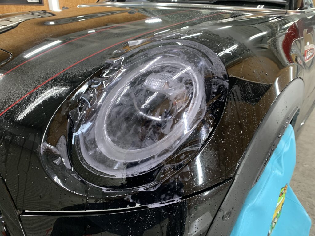MINI JCWのヘッドライトにプロテクションフィルムを施工している様子。施工液を使用しながら貼り込みを行う工程