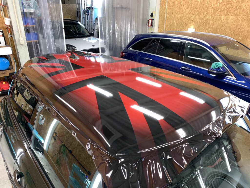 MINI F56 JCWのルーフへ、CABANAデザインをモチーフにしたユニオンジャック柄ラッピングを施工している様子。レッドとブラックを組み合わせた大胆なデザインをルーフ全面へ施工し、MINIらしい個性的なスタイルへカスタムしている。