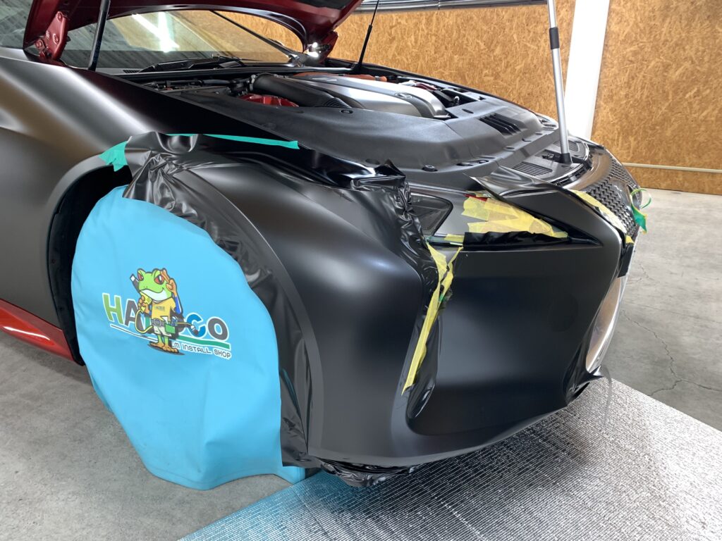 レクサスLC500hのフロントバンパーへ3Mサテンブラックを施工中。複雑な曲面へ丁寧にラッピングを行っている様子。