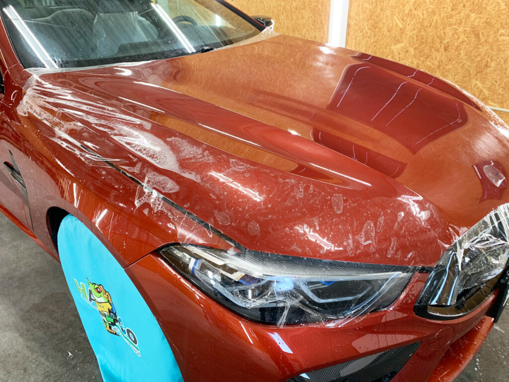 BMW M8のボンネットへプロテクションフィルムを施工している様子。一部スキージー作業が完了し、施工液が抜けたことでフィルムがボディへ密着している施工途中の状態。