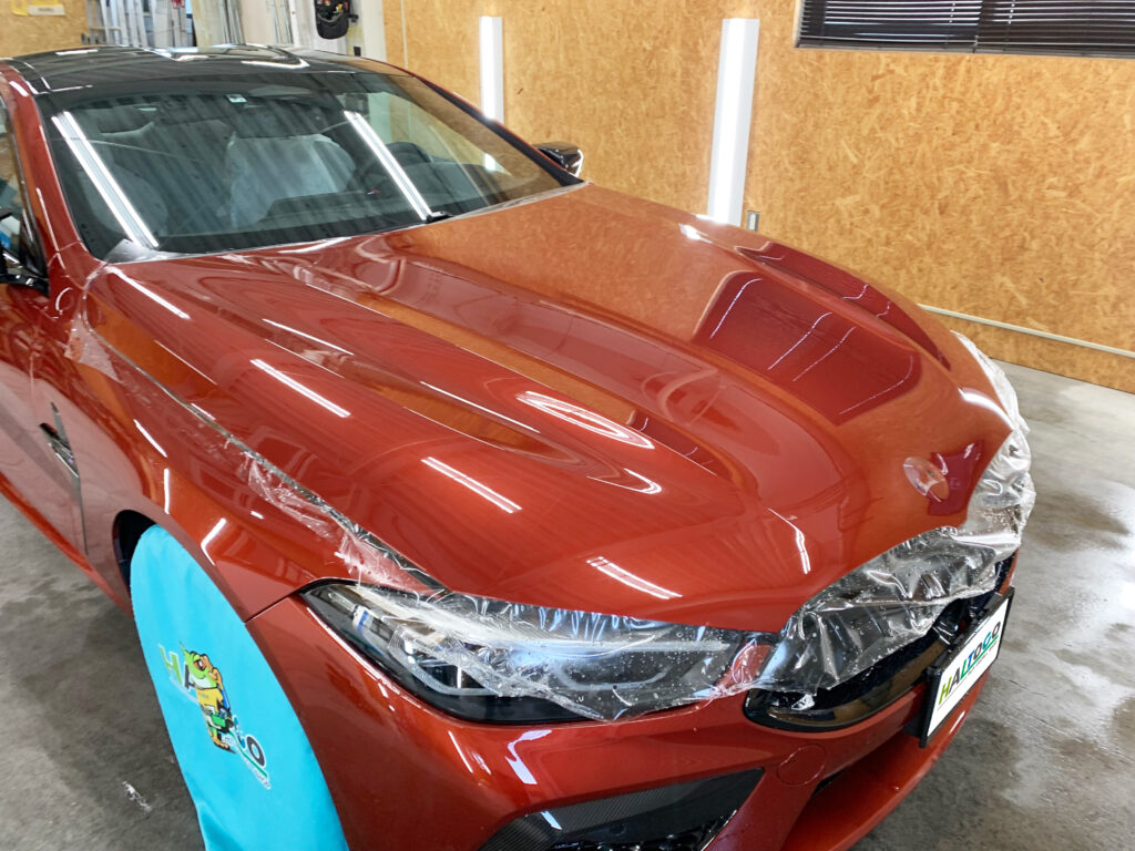 BMW M8のボンネットへプロテクションフィルムを施工中の様子。スキージー作業で施工液を抜き終え、フィルムがボディ形状へしっかり密着した状態。