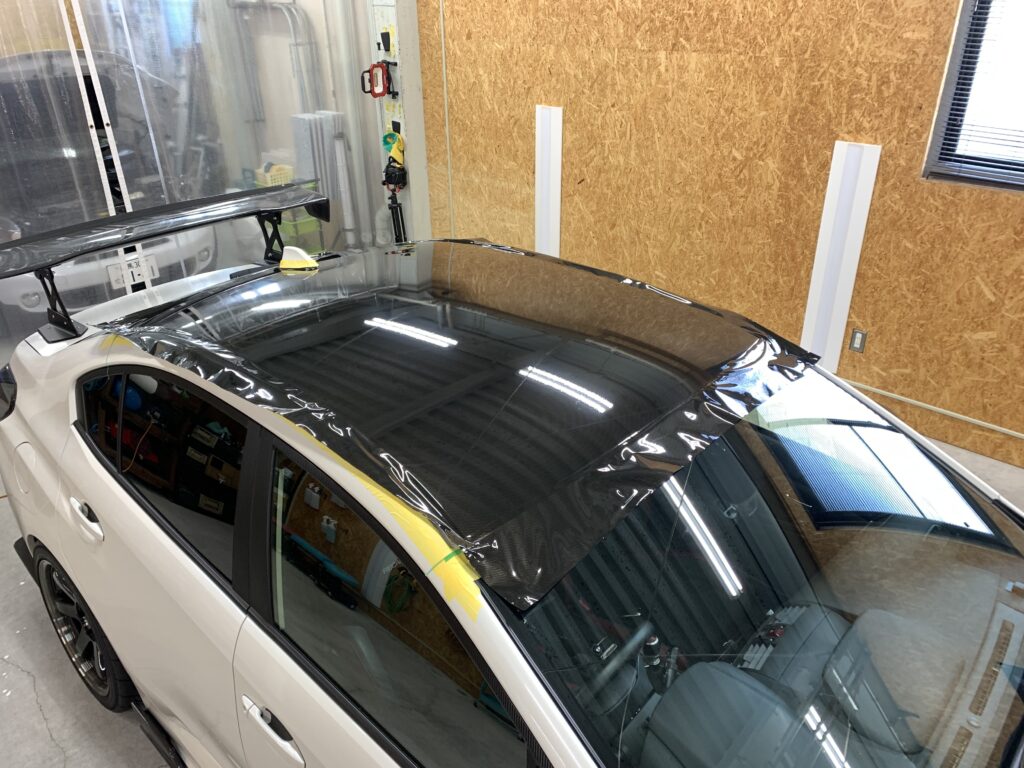 スバルWRXのルーフへTECKWRAP RCF03カーボン調ラッピングフィルムを貼り込んでいる施工途中の様子。