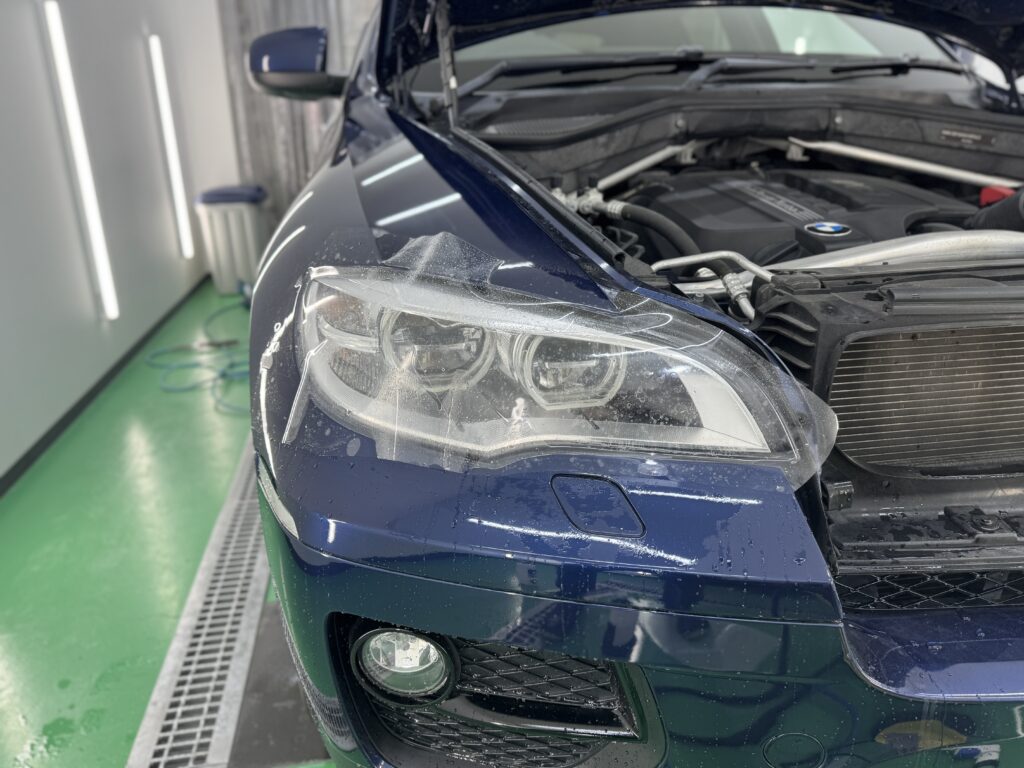 BMW X6のヘッドライトにプロテクションフィルムを貼り込んでいる施工中