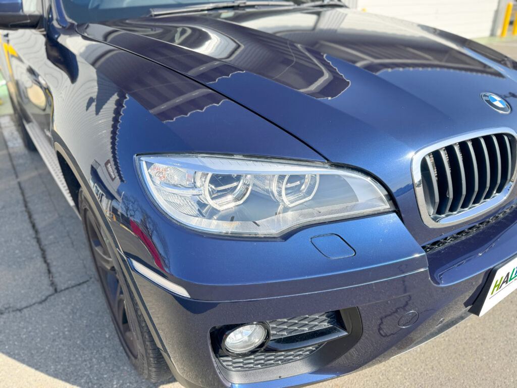 BMW X6のヘッドライトリペア完成後、屋外で透明感のある仕上がりを確認できるアップ写真