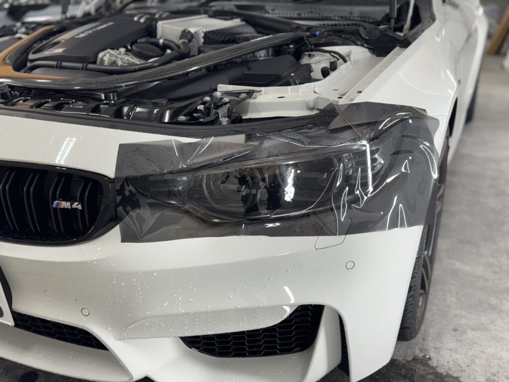BMW M4のヘッドライトにダイヤモンドスウェル・ブラックブラウンを施工している様子