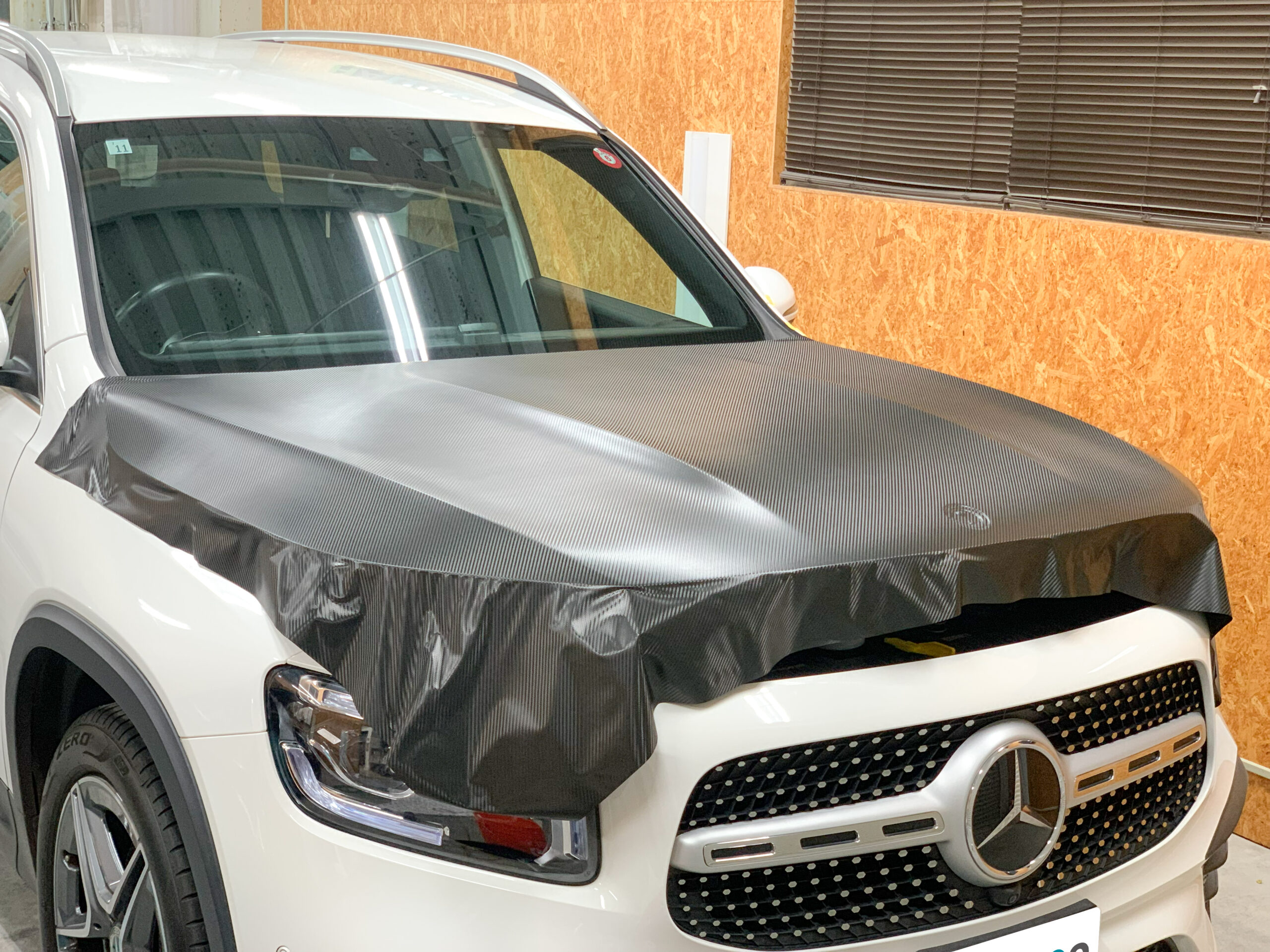 Mercedes-Benz GLB200dのボンネットへ3Mカーボン調ラッピングフィルムを施工している様子