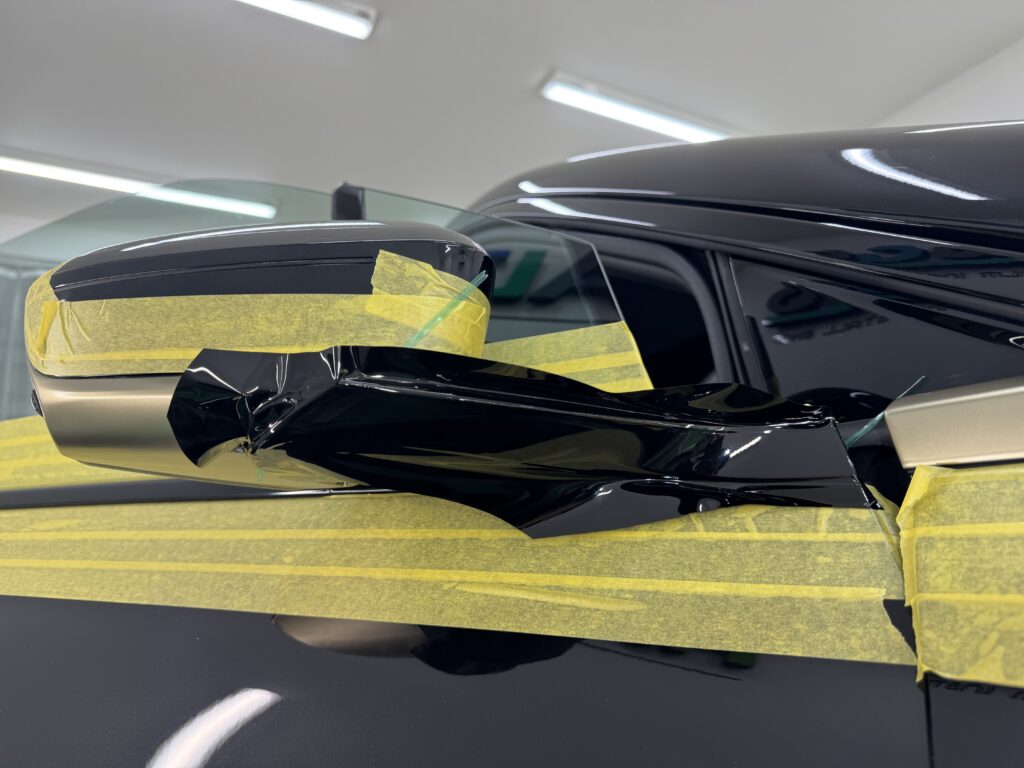 BMW iXフロントドアミラー付近のモールをブラックアウトラッピング施工中