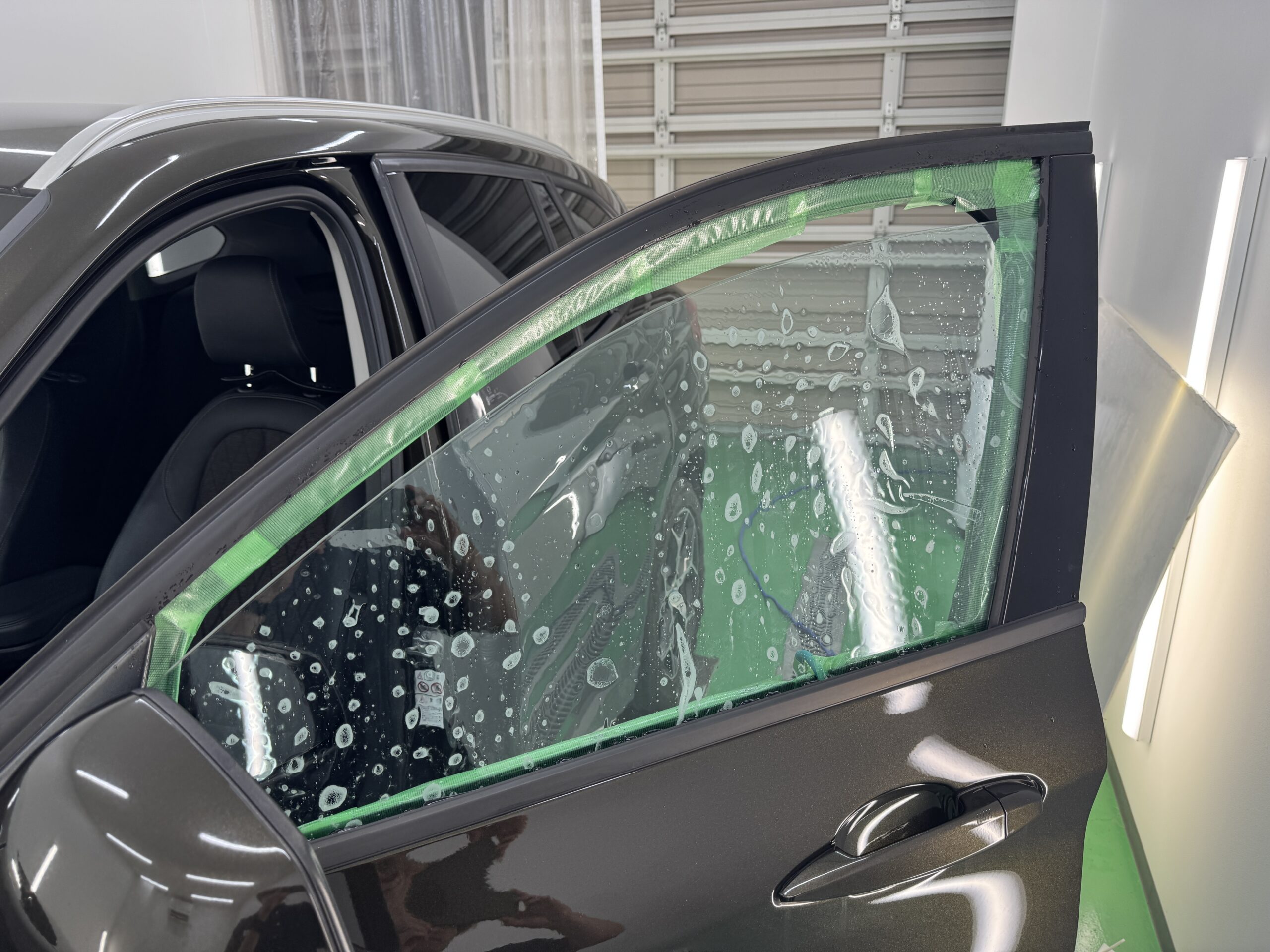 BMW X1のフロントドアガラスを養生して透明断熱フィルム施工の下準備をしている様子