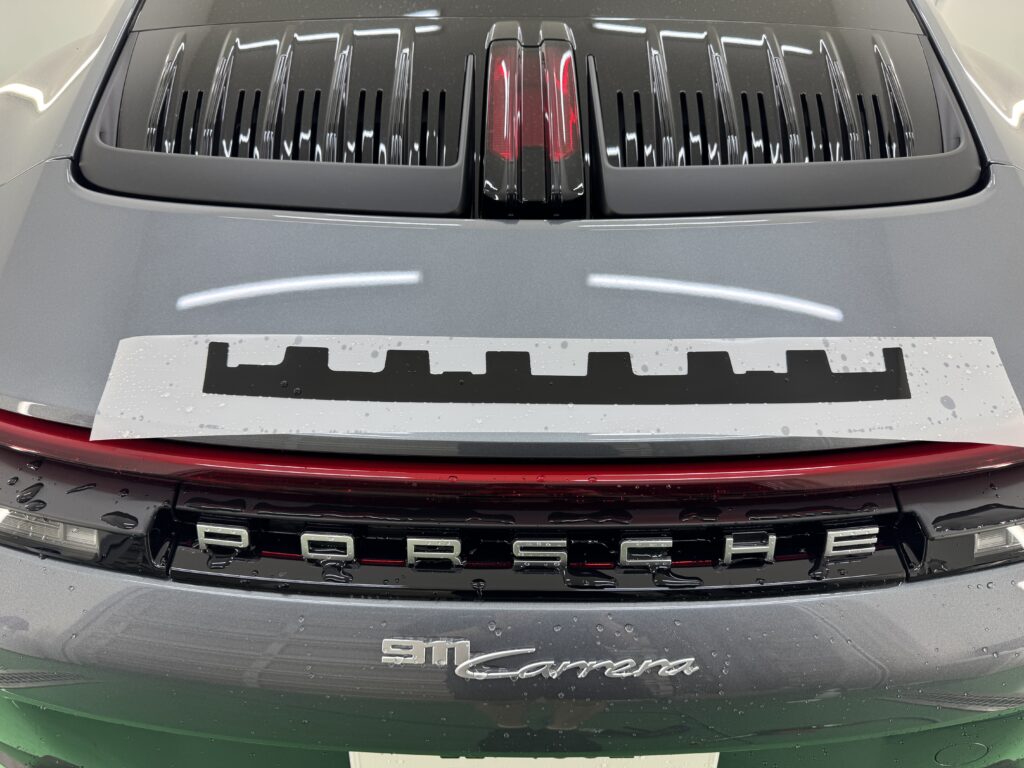 ポルシェ911 CarreraのリアガーニッシュにグロスブラックカラーPPFを施工する様子