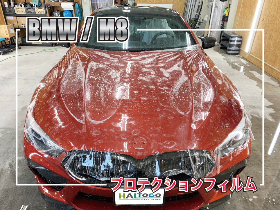 BMW M8のボンネット全体に透明プロテクションフィルムを施工中の様子。大型ボンネットへ丁寧にフィルムを位置合わせしている施工工程。