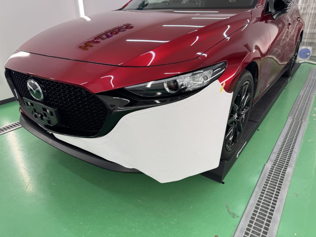 MAZDA3のフロントバンパーに版下を合わせて形状を確認している様子