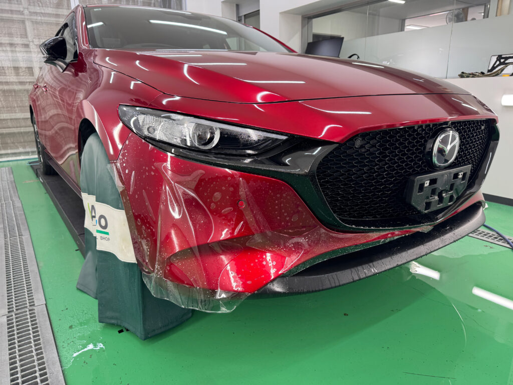MAZDA3のフロントバンパー下部に透明PPFを貼り付けている途中の様子
