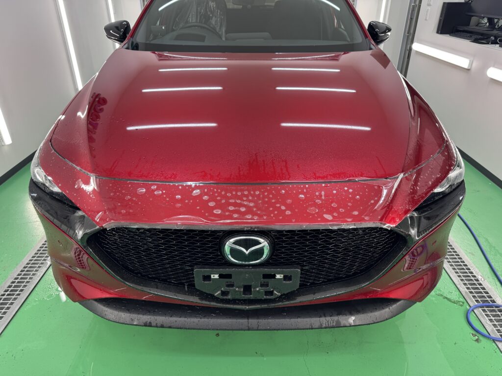 MAZDA3のフロントバンパー上部に透明PPFを配置した施工途中の様子