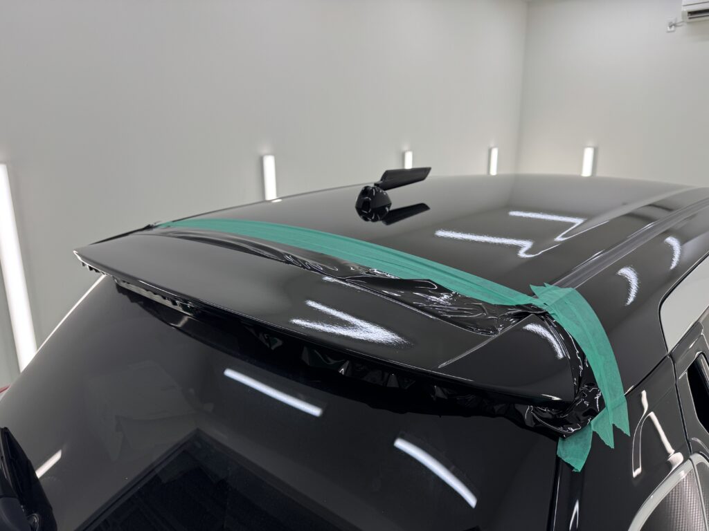 スズキ スイフトのリアウィングにグロスブラックフィルムを施工している様子